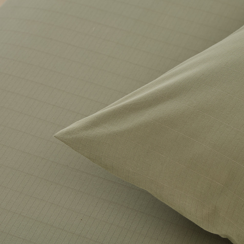 Olive green pillowcases on bed with organic grounding sheet – calming earth tone wellness bedding by Terra Solum